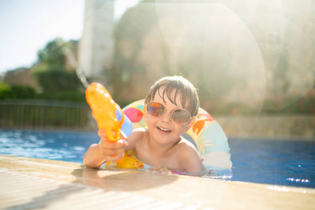 Cute child in floating ring plays with water gun in pool