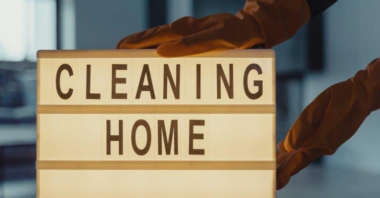 Latex-gloved hands holding a lightbox sign with 'CLEANING HOME' text.