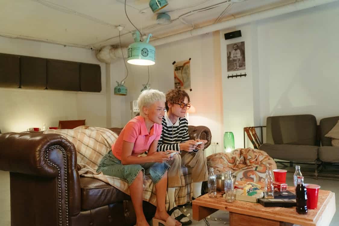 Free Teenagers enjoying a retro gaming session in a cozy, dimly-lit basement room. Stock Photo