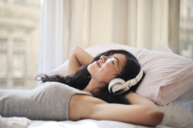 Free A woman with headphones lying on a bed, enjoying music in a relaxed, cozy setting. Stock Photo