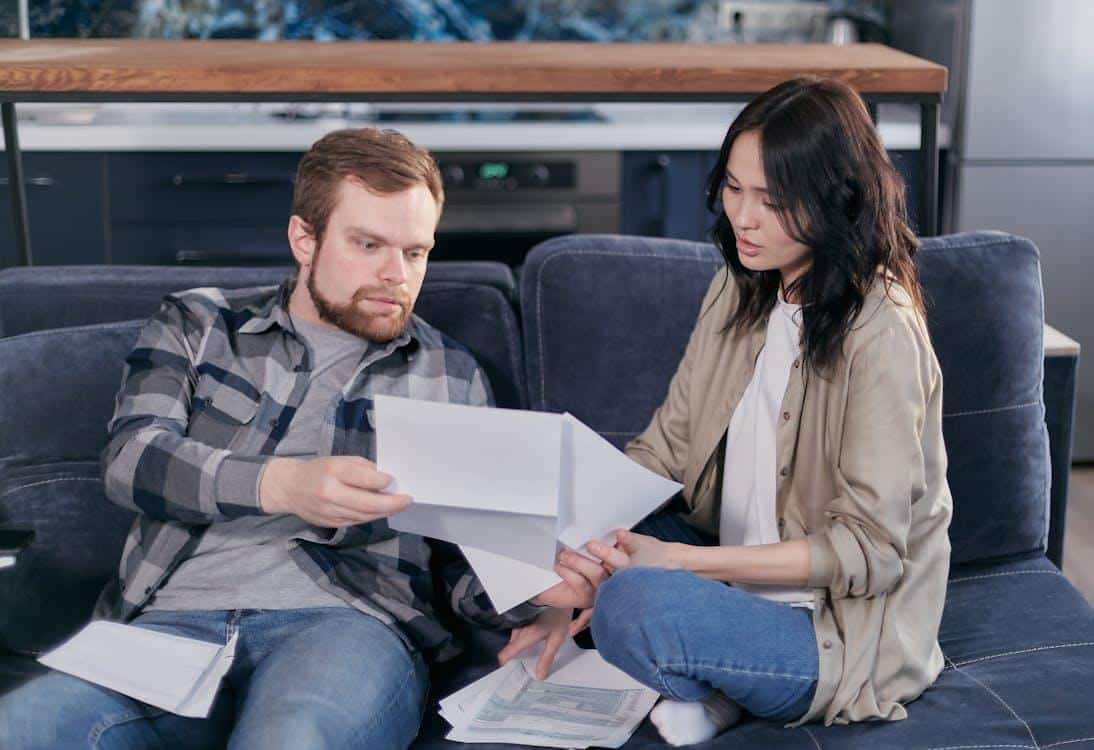 Free Asian woman and Caucasian man discussing taxes on couch. Stock Photo