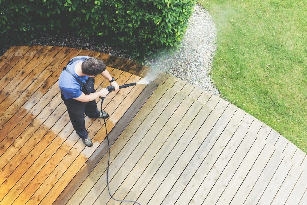 A man jet spraying water on outdoor wooden deck